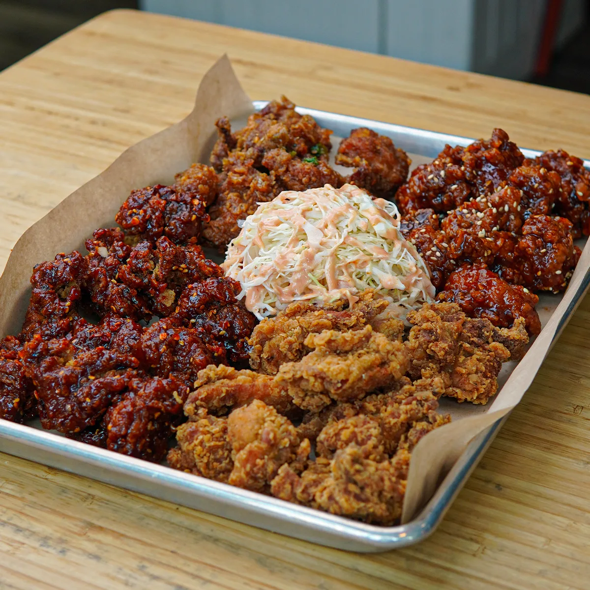 A tray of Korean fried chicken in four different glazes with coleslaw in the middle