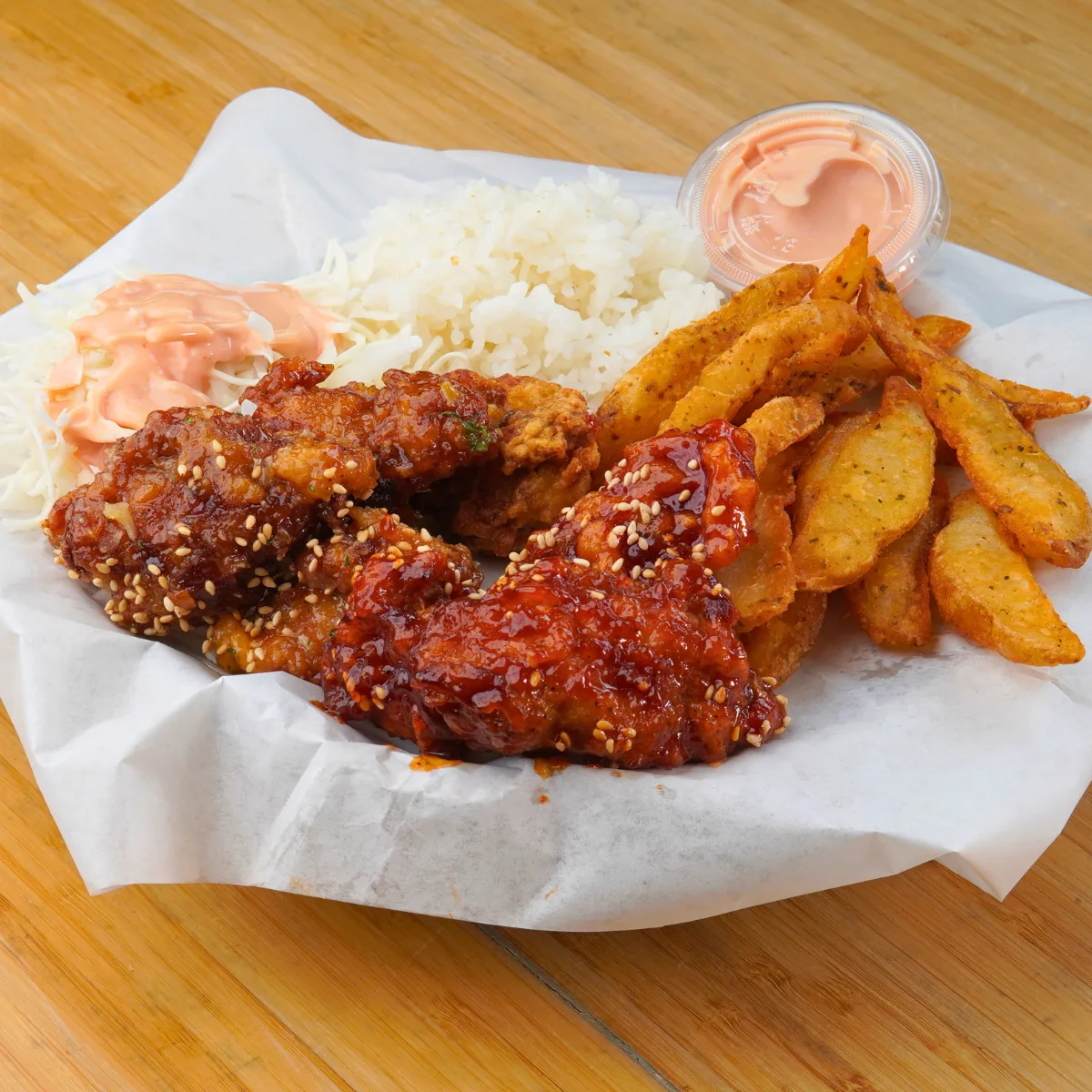 Glazed Korean fried chicken with rice, coleslaw and potato wedges on paper