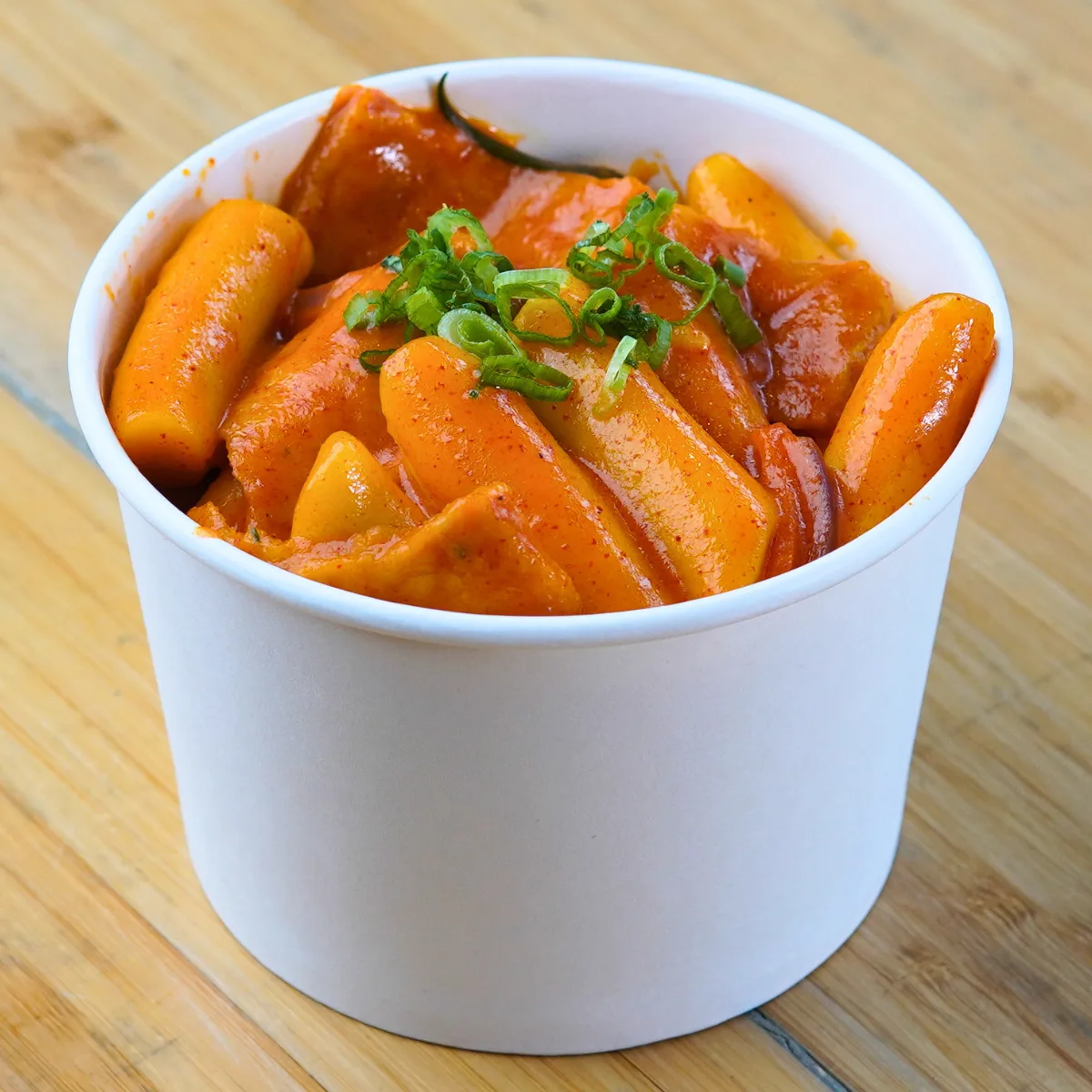 A tub of rice cakes in creamy rosé sauce topped with spring onion